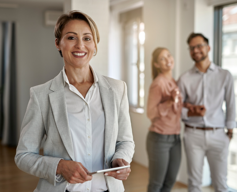 real estate agent standing and smiling in front of new couple homebuyer