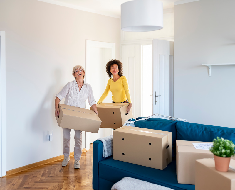 two women carrying boxes in new home