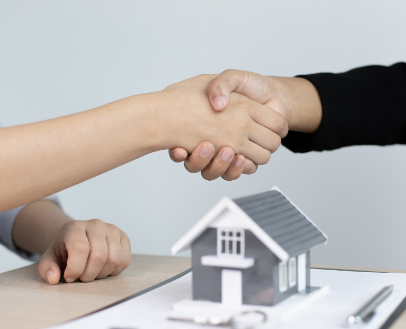 shaking hands of real estate agent and home buyer with small house model
